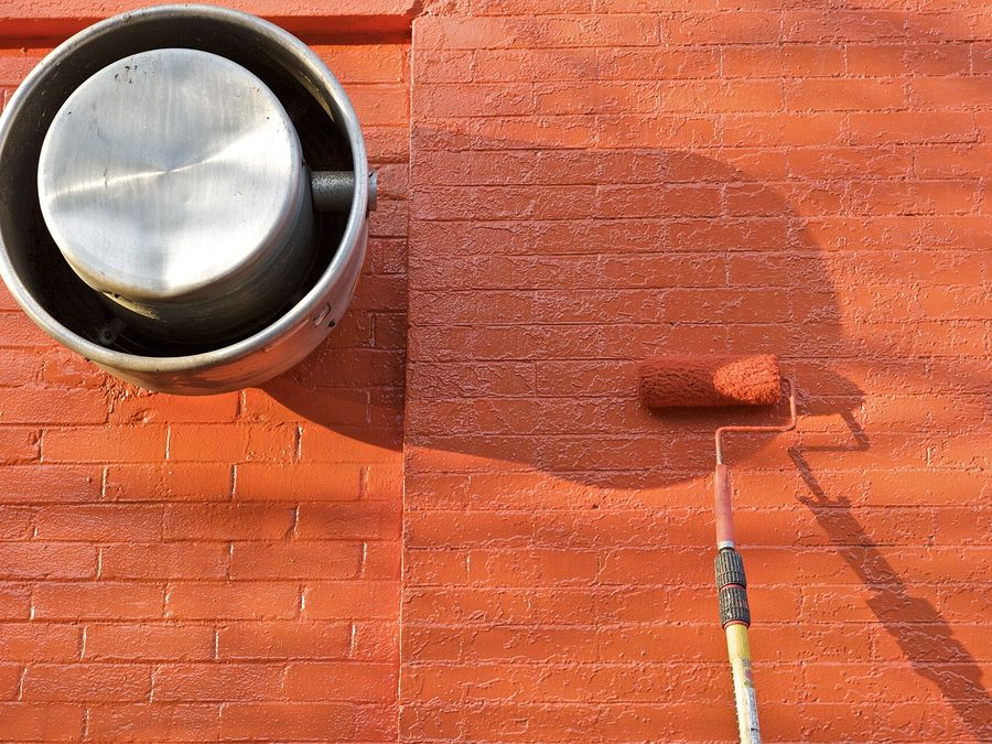 Paint roller applying fresh orange paint to a brick wall